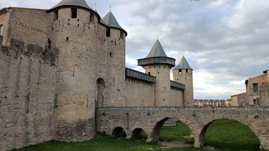 Pont d'entrada, amb fossat a sota ple de gespa i muralla amb torres de Carcassonne.