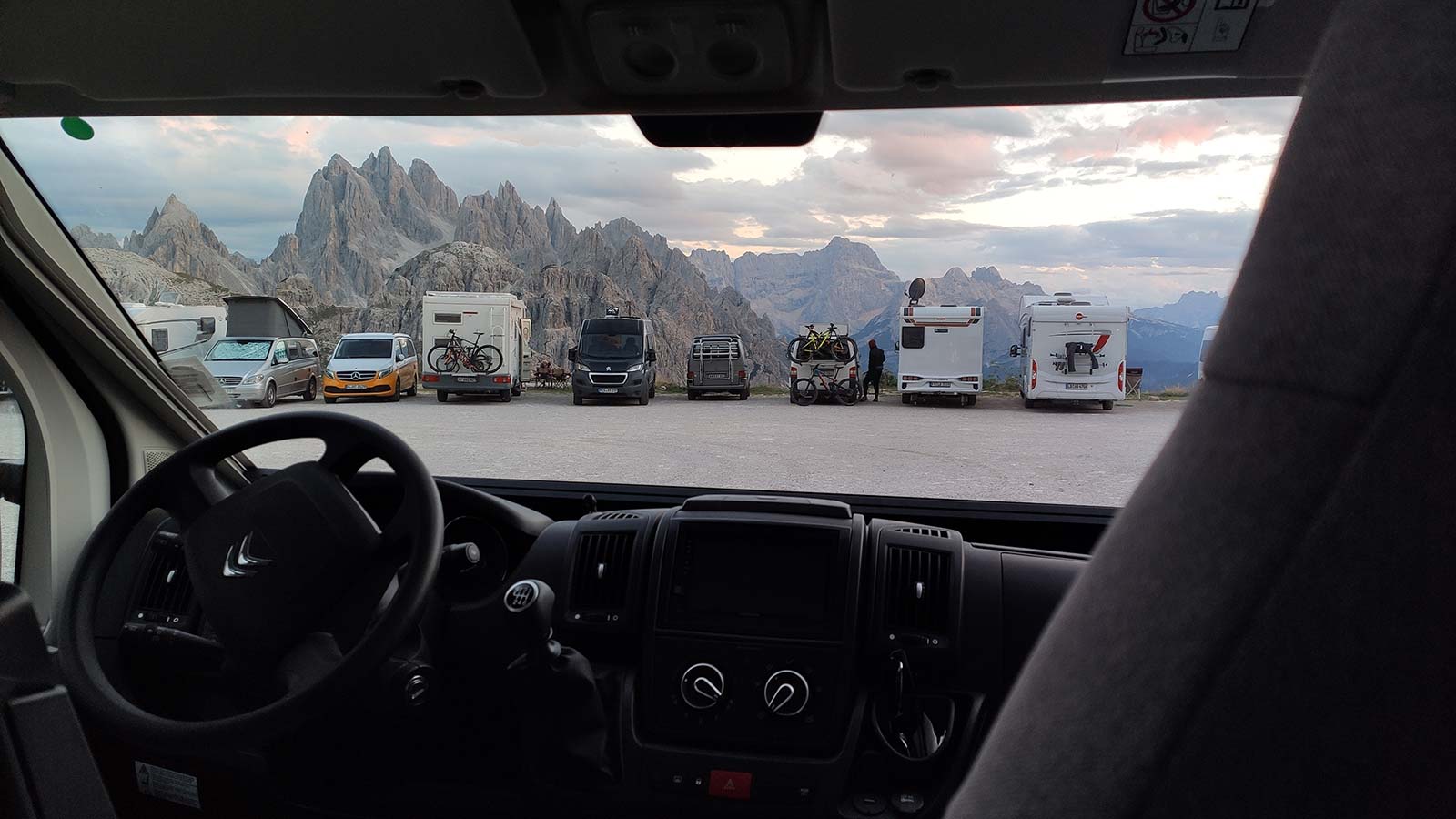 Foto on es pot veure el tablier e la càmper i a través del vidre autocaravanes i altres furgonetes aparcades al peu d'una muntanya.