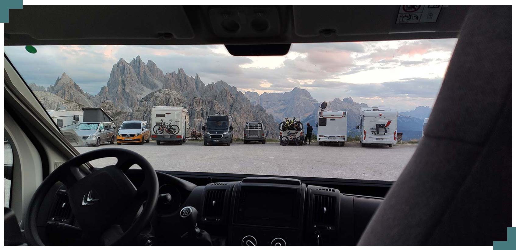 Foto on es pot veure el tablier e la càmper i a través del vidre autocaravanes i altres furgonetes aparcades al peu d'una muntanya.